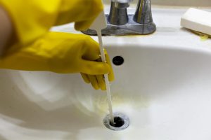 A person is trying to unclog the drain of a sink using plastic disposable snake auger tool which helps pull hair and soap debris from the sinkhole. Close up DIY home maintenance concept.