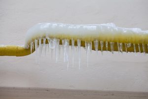 Icicles hanging from a frozen water jets, tube, yellow pipe. aged wall background. winter time concept.