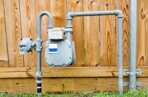 Natural gas meter in residential suburban backyard with wooden fence in background.